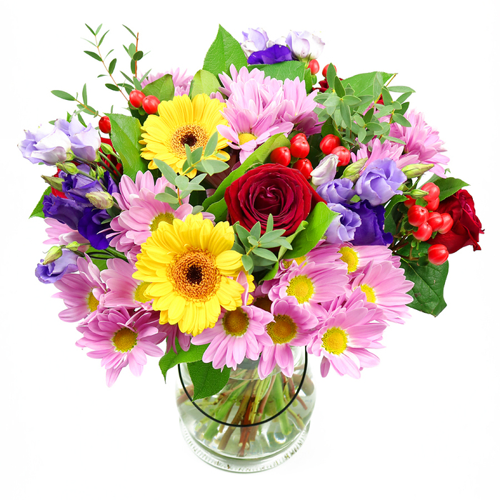 In this photograph, a richly coloured bouquet fills a clear glass vase, standing alone against a bright white backdrop that makes every detail easy to pick out. The central flowers are lush, deep red roses, their petals closely layered in soft spirals that suggest depth, warmth, and a touch of timeless romance. On either side, two vivid yellow gerbera daisies with dark brown-orange centres brighten the design, their broad, circular faces and radiating petals creating an instant feeling of sunshine and optimism. Surrounding this central group, clusters of soft pink daisies or chrysanthemums stretch outward, each bloom a delicate ring of slender petals around a tiny yellow centre, together providing a gentle, soothing frame of colour. Purple and lavender lisianthus stems weave gracefully through the pink and yellow blooms, their bell-shaped flowers slightly frilled at the edges, adding cool elegance and a sense of flow and movement. Tucked between petals, bright red hypericum berries form small, rounded bunches that introduce a glossy texture and an extra spark of colour, like tiny jewels scattered through the bouquet. Mixed green foliage-from broader, darker leaves to fine, airy sprigs-surrounds and supports the flowers, giving the arrangement fullness and a fresh, garden-like character. The clear vase reveals a tidy bundle of cut stems resting in clean water, highlighting the care and skill involved in preparing the bouquet. Altogether, the arrangement feels joyful and welcoming, the kind of bouquet that could sit in the window of a flat above a shop on Gerrard Street, decorate a cosy corner near Shaftesbury Avenue, or be delivered for a birthday celebration in Chinatown, bringing a burst of floral colour and calm into the heart of the busy city.