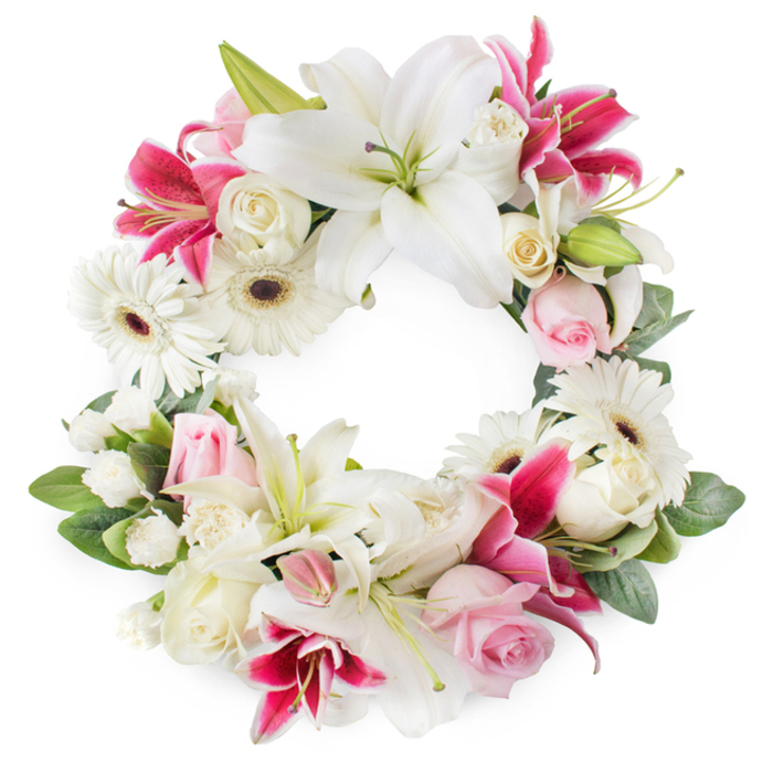 An open round wreath of condolence flowers is displayed front-on against a bright white background, giving the impression of a soft, floral circle suspended in light. The colour palette is a careful blend of whites, blush pinks, and saturated fuchsia tones, creating a balanced composition that feels both refined and expressive. Large white lilies are spaced around the ring as main focal points, their broad petals slightly ruffled at the edges and their centres marked with green pistils and golden-tipped stamens. Between them, deep pink and magenta lilies unfurl, with petals that may show subtle freckles or shading, adding a more dramatic hue that threads through the design like a ribbon of colour. Crisp white gerbera daisies with dark brown to almost black centres add structure and a fresh, clean aesthetic, their orderly petals giving a sense of modern simplicity. Nestled among these are clusters of soft pink roses and creamy white roses, some blooms tight and others opening, their layered petals providing a plush, velvety texture that softens the transitions between flowers. Smaller white accent flowers, such as miniature carnations or sprays, are woven throughout the circle, filling tiny spaces so the wreath appears full, cohesive, and comforting. A generous foundation of green foliage wraps around the ring, leaves overlapping and gently protruding, adding depth, shadow, and a natural garden-like feel. The open centre of the wreath symbolises continuity and the ongoing cycle of life, a sentiment that resonates during funerals and memorial services. In the context of London's Chinatown, this could be the sort of wreath delivered by a local florist to a family observance, a temple service off Gerrard Street, or a remembrance gathering near Leicester Square, conveying heartfelt condolences with grace and quiet beauty.