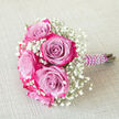 On a background of pale, textured beige fabric-soft and understated like handmade paper-this carefully crafted bouquet appears calm yet full of emotion, as if set aside for a moment of stillness before a celebration in Chinatown. At its core, several large roses display a captivating gradient of colour: the innermost petals glow in cool lavender and lilac hues, gradually transitioning into a vivid ring of fuchsia and bright magenta at their gently ruffled edges. These bi-colour blooms feel lush and velvety, balanced perfectly between openness and structure. Interwoven among the roses, airy stems of white baby's breath create feathery clouds of tiny blossoms. The gypsophila softens the composition, adding a classic, almost nostalgic bridal quality that contrasts gracefully with the modern drama of the rose colours. The stems are bound together with a deep purple satin ribbon, neatly wrapped and smooth under the hand, suggesting the practiced technique of a skilled florist. Winding in an elegant spiral over the ribbon, a string of luminous white faux pearls adds a jewellery-like detail, reminiscent of the delicate accessories often chosen for weddings and engagements around Gerrard Street and Wardour Street. The bouquet lies diagonally, with its pearl-adorned handle directed toward the right side of the image, hinting that it is ready to be lifted and carried down an aisle or into a city hall ceremony. The overall impression is of romantic refinement and intentional design, ideal for weddings, proms, or intimate celebrations that unfold in and around London's Chinatown, where tradition and contemporary style meet so effortlessly.