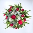 From a high, top-down view, this luxurious round bouquet fills the entire frame, set against a clean white background that makes every colour sing. At the centre, velvety deep red roses, some still in tight bud and others gently unfurling, create a romantic heart to the arrangement, their petals layered and soft as silk. Around them, rich fuchsia and ruby-red carnations with frilled, ruffled edges add fullness and a sense of joyful celebration, the kind of flowers you might carry down a busy Chinatown side street after a special dinner. Threaded between the red blooms are clusters of crisp white spray chrysanthemums, each daisy-like flower with a bright yellow-green centre that lifts the palette and adds a cheerful, almost sparkling contrast. Wisps of tiny white gypsophila-baby's breath-drift through the bouquet like a light mist, softening the transitions between flowers and giving the design a cloud-like delicacy. Lush greenery radiates outward, with strong, pointed dark green leaves providing structure, and rounded, silvery eucalyptus leaves weaving through for a cool, contemporary touch and a hint of fresh, herbal scent. The lighting is even and natural, highlighting the natural gloss of the foliage and the velvety texture of the petals without harsh shadow. The composition feels generous, balanced, and carefully hand-crafted, just like a bouquet you might have delivered across Chinatown to mark an anniversary, a birthday, or to send a heartfelt get-well wish. It visually conveys affection, gratitude, and warmth, as if it has just been lifted from a florist's workbench, ready to surprise someone at their front door.