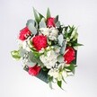 A hand-tied bouquet brimming with red and pink roses, velvety red carnations, and soft white daisies is captured in gentle daylight, the flowers gathered closely together like a bright morning unfolding over Chinatown. The roses sit proudly at the heart of the arrangement, their petals full and layered, while the carnations add ruffled depth, each fold catching the light with a warm, almost feathery softness. Around them, daisy-style white chrysanthemums and tiny clusters of gypsophila glow like scattered snowflakes, softening the intense reds with a clean, luminous contrast. Eucalyptus stems curl through the bouquet in cool, silvery greens, their rounded leaves adding a modern, urban edge reminiscent of the calm corners around Gerrard Street or Newport Place after the rush of the day. Deeper tropical foliage fans out at the base, glossy and rich, creating a structured frame that keeps the bouquet feeling both generous and tidy. The overall shape is rounded yet relaxed, suggesting the confident touch of an experienced florist who knows how to balance colour, texture, and space so each bloom can breathe. This arrangement looks perfect for a low coffee table in a Chinatown apartment or as a welcome-home surprise carried along Wardour Street, radiating joy, affection, and a sense of fresh beginnings. One can almost sense the mingled scent of rose, carnation, and eucalyptus drifting gently through the room, turning an ordinary corner into a small celebration of colour and care.