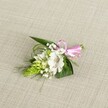 A delicately handcrafted boutonniere rests on a softly textured, light beige linen-style cloth, the neutral background allowing every petal and leaf to stand out with quiet clarity. At the heart of the design sits a single open white alstroemeria, sometimes called a Peruvian lily, its broad petals gently ruffled at the edges and brushed with fine reddish-brown speckles close to the throat. The flower feels freshly picked, with stamens clearly visible in the centre, suggesting the crisp, almost green sweetness of a just-cut bloom. To the left, a compact lime-green spike of tightly packed buds, reminiscent of Ornithogalum or a ginger-like flower cluster, adds an intriguing sculptural touch and a burst of vivid colour. Around these focal elements, sprays of classic white baby's breath float like tiny clouds, softening the outline and bringing an airy, romantic lightness that would suit any Chinatown wedding or prom along nearby Gerrard Street. A base of foliage anchors the piece: broad, dark green, sword-shaped leaves provide structure, while fine strands of grass-like greenery curve and twist playfully, adding movement and texture. At the right-hand side, the stems are neatly gathered and finished with a small, glossy pastel pink satin ribbon bow, its smooth sheen catching the even, gentle light. The overall mood is tender and celebratory, evoking the calm anticipation of getting ready on a special morning in central London. This small floral accessory looks ready to be pinned to a lapel or worn on the wrist, a thoughtfully designed finishing touch that blends white, green, and pink into a timeless, elegant corsage or buttonhole.